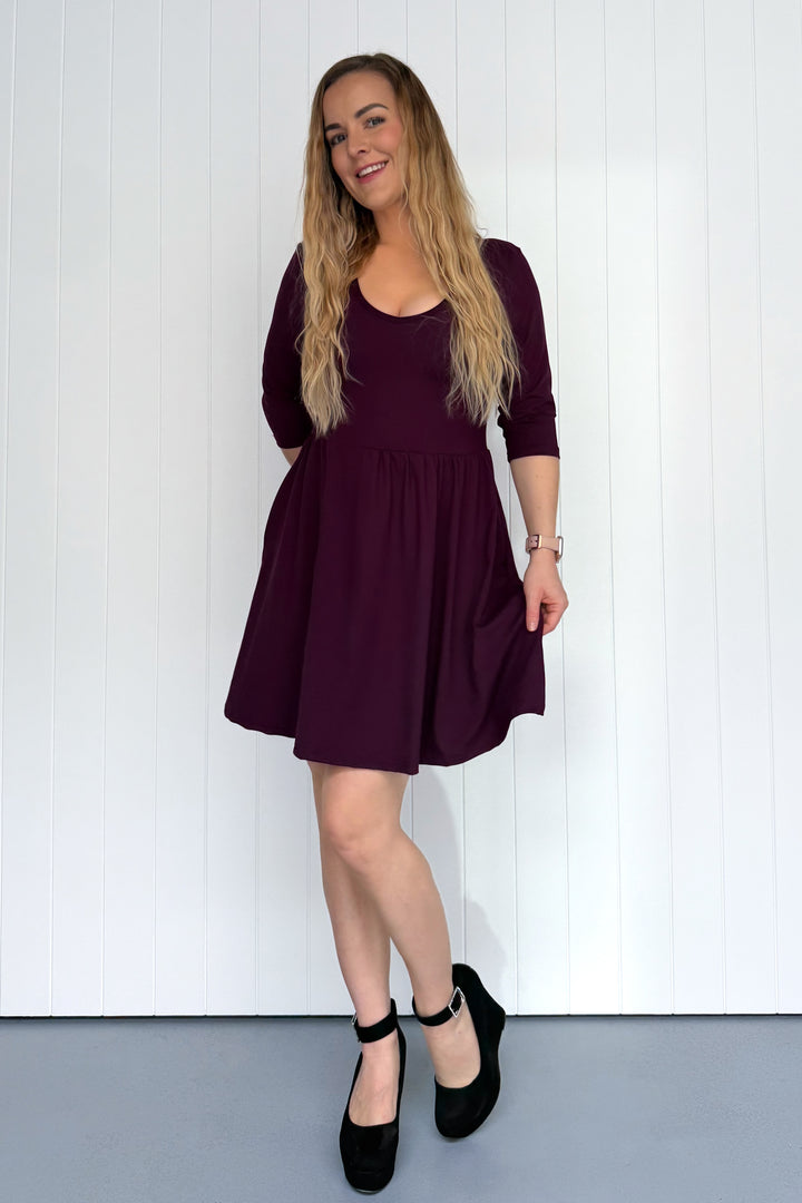 Woman wearing a purple dress standing against a white wall.