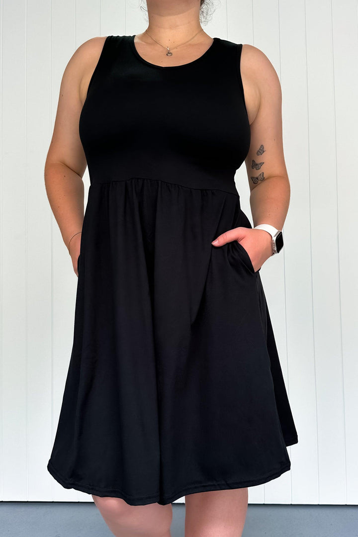 A model wearing a black sleeveless knee-length dress with a V-neck and side pockets.