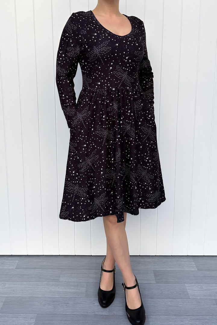 Black dress with white pattern worn by a person against a white wooden panel background