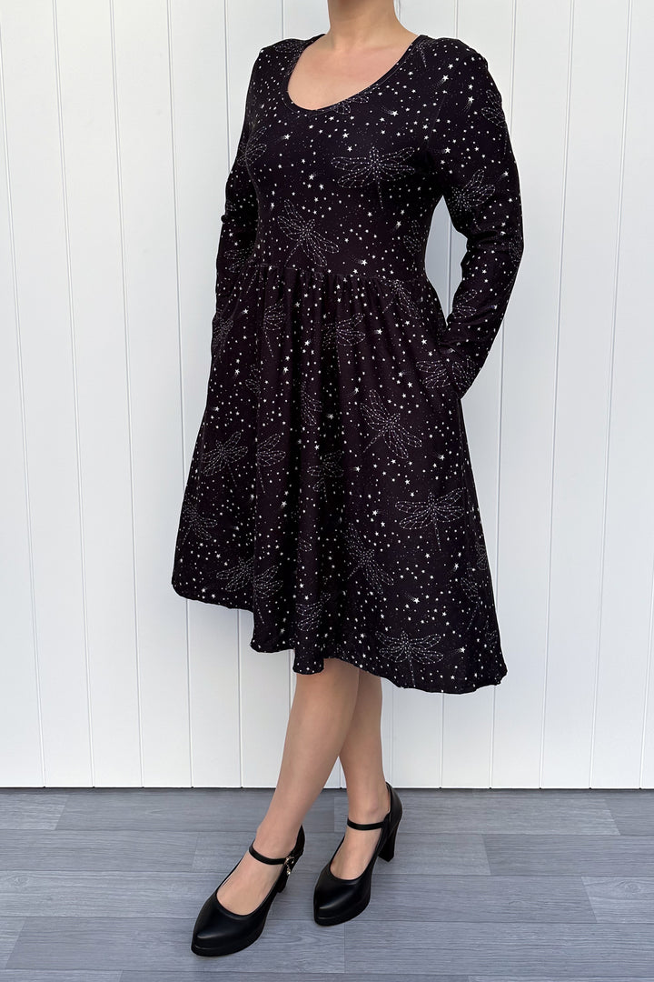 Person wearing a black dress with white patterns against a white wooden panel background