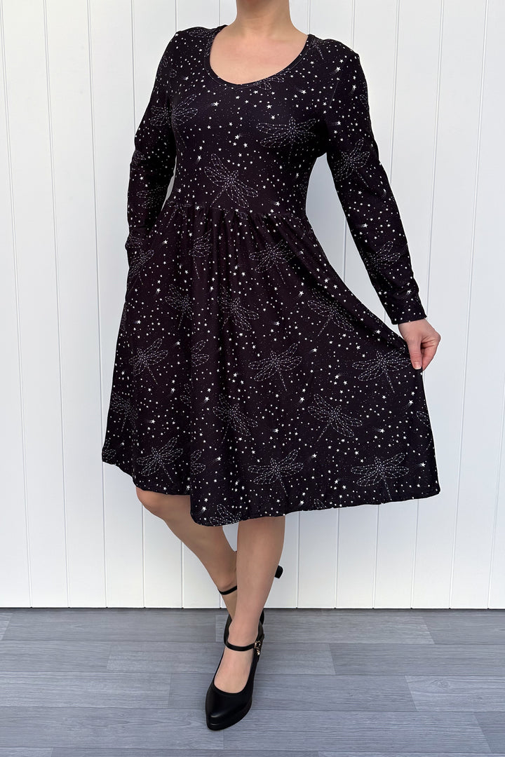 Person wearing a black dress with white dragonfly patterns against a white wooden panel background