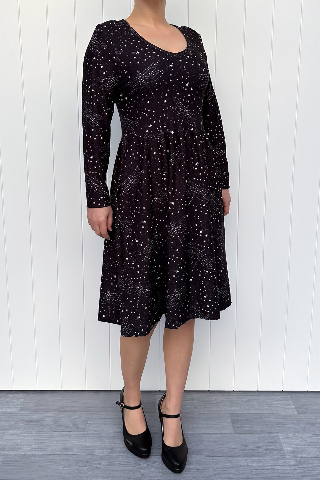 Person wearing a black dress with white dragonfly patterns against a white wooden panel background