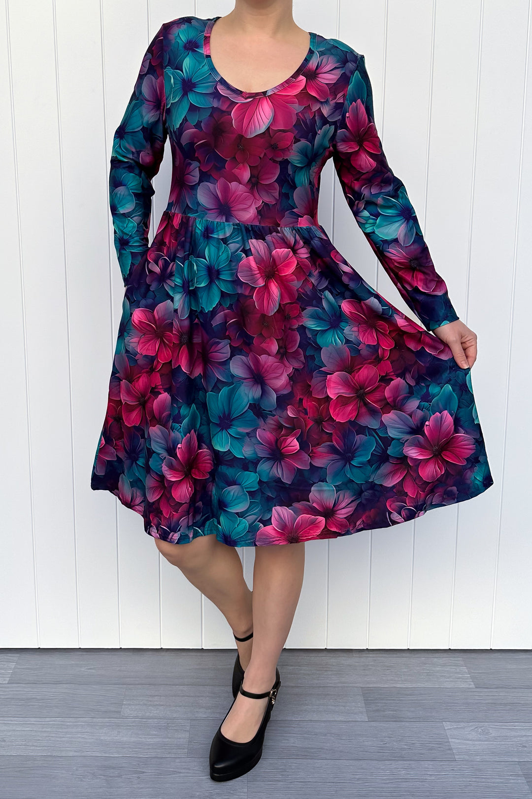 Woman wearing a colorful blue and red floral dress against a white wooden panel background