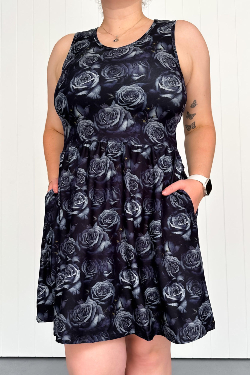 A sleeveless mini dress with a dark rose floral pattern and pockets, worn by a model.