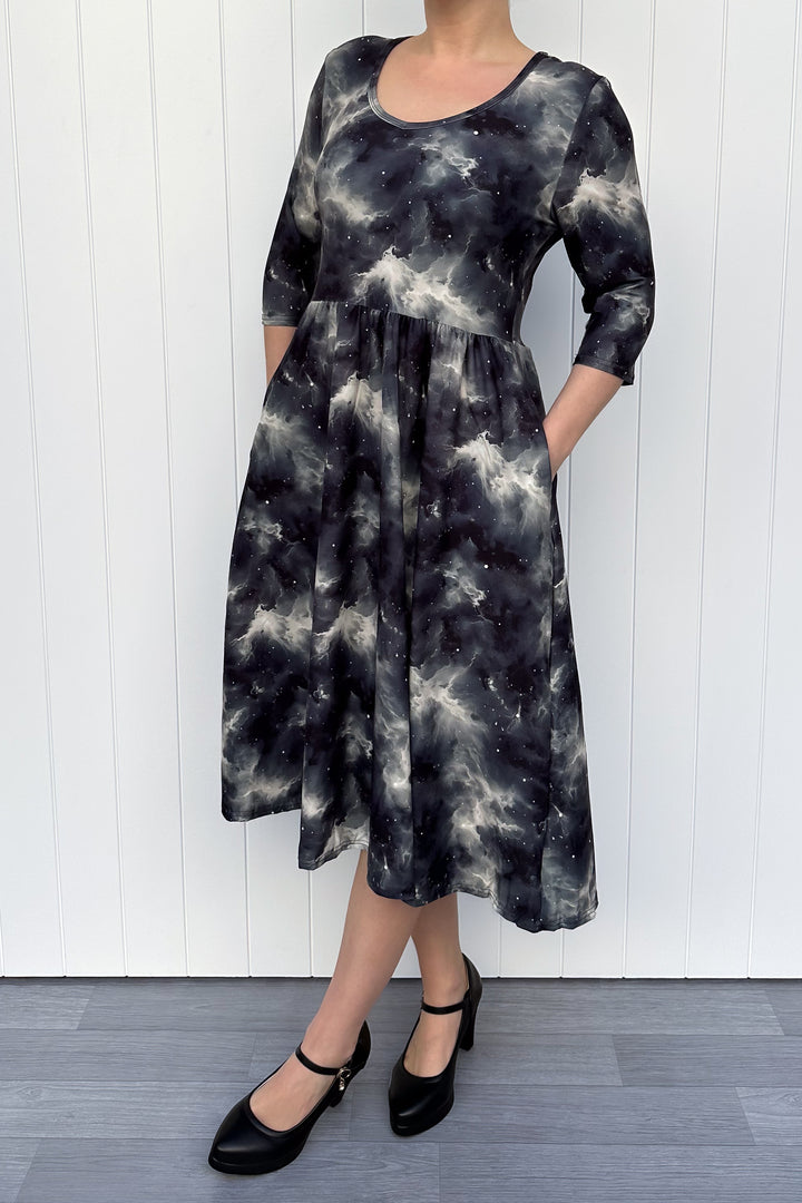 Person wearing a black and gray tie-dye dress against a white wooden panel background