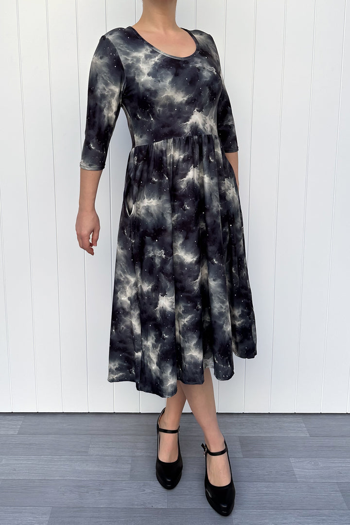 Person wearing a black and gray tie-dye dress against a white wooden panel background