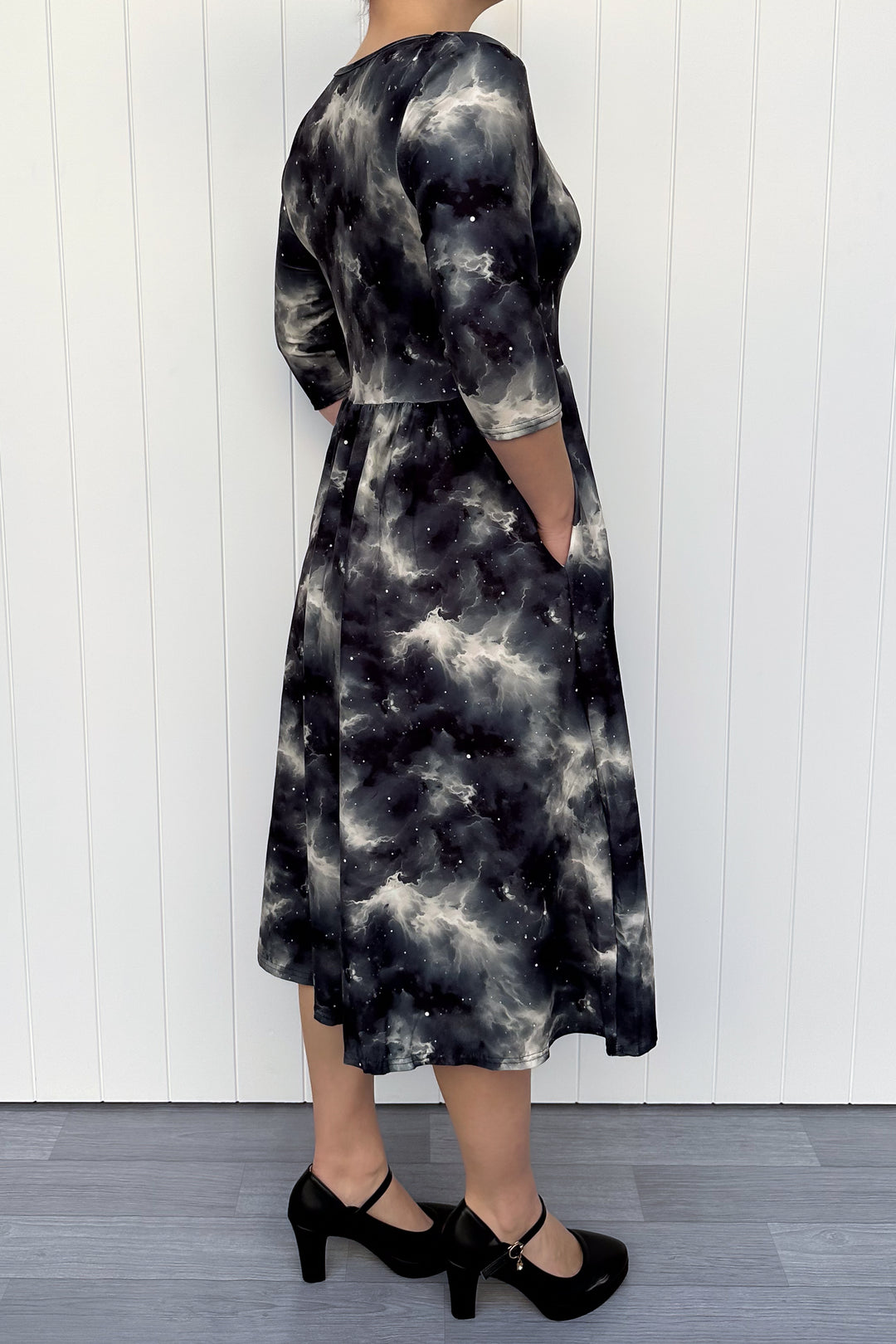 Person wearing a black and white tie-dye dress against a white wooden panel background