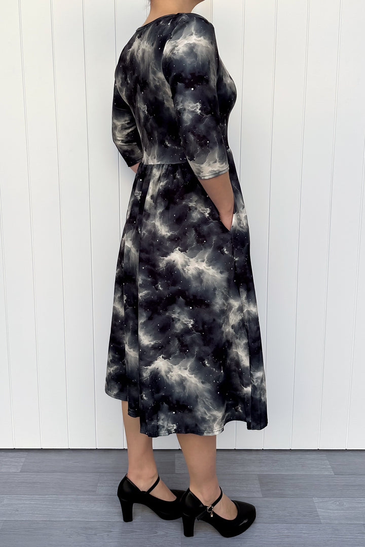 Person wearing a black and white tie-dye dress against a white wooden panel background