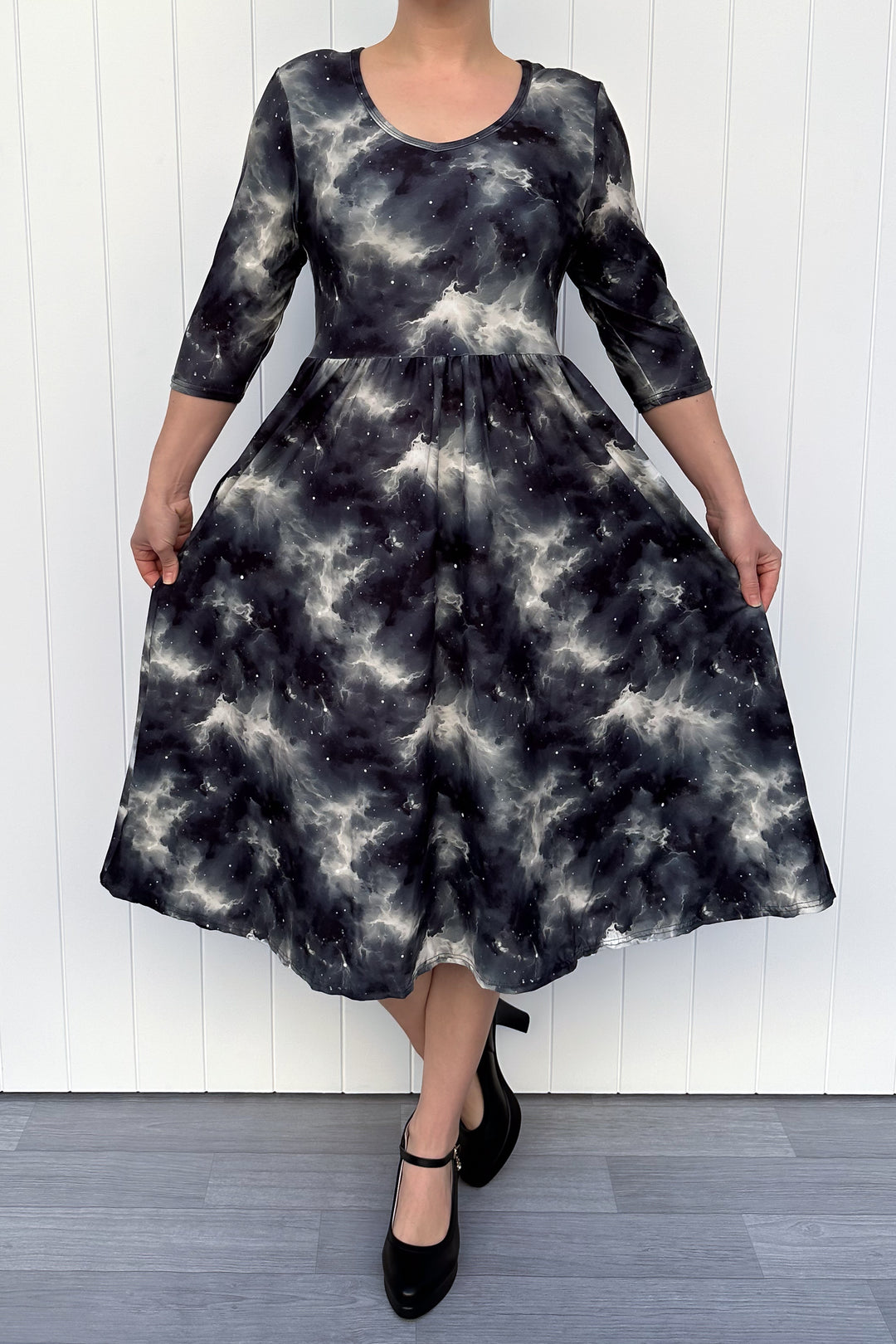 Person wearing a black and white patterned dress against a white wall.