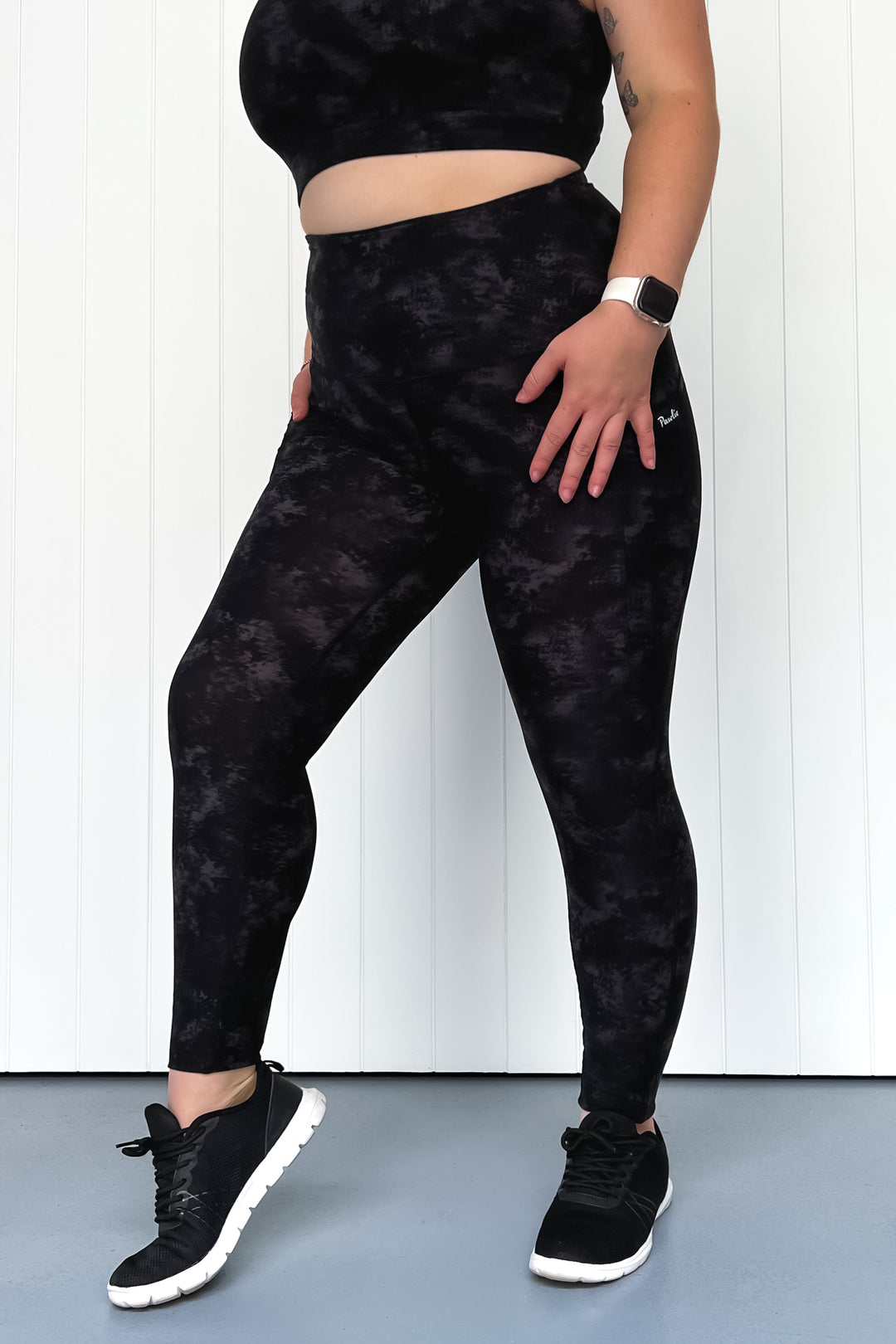 Person wearing black tie-dye leggings and black sneakers on a white background