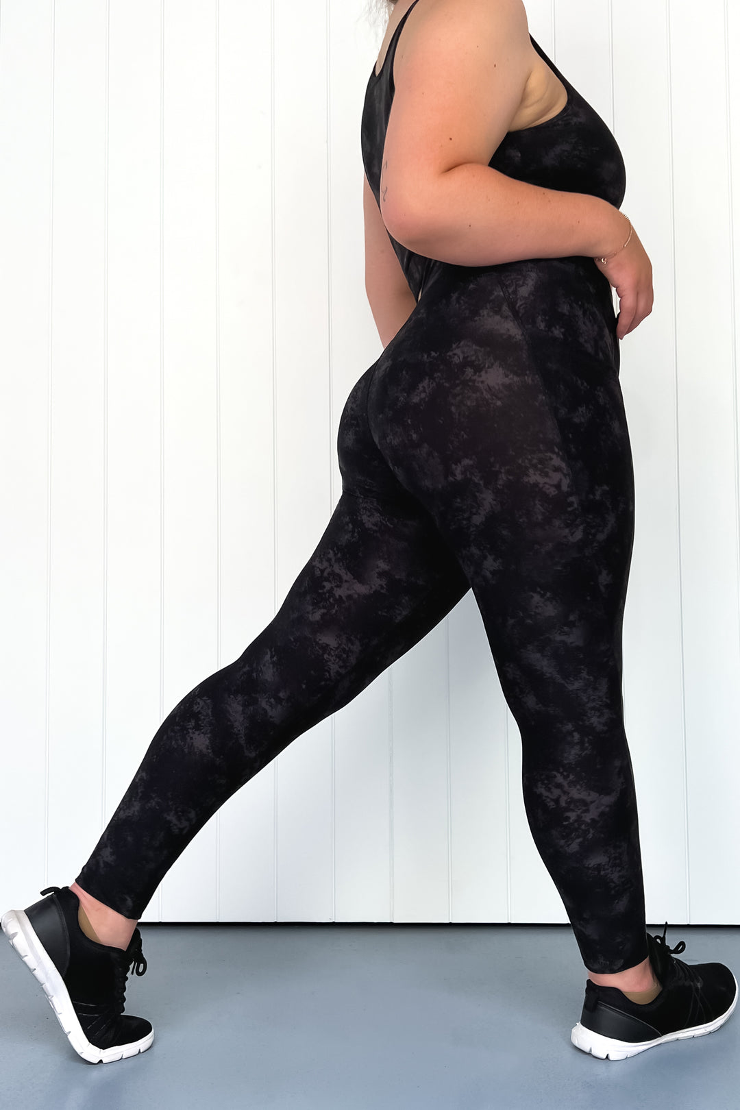 Person wearing black tie-dye leggings and black sneakers on a white background