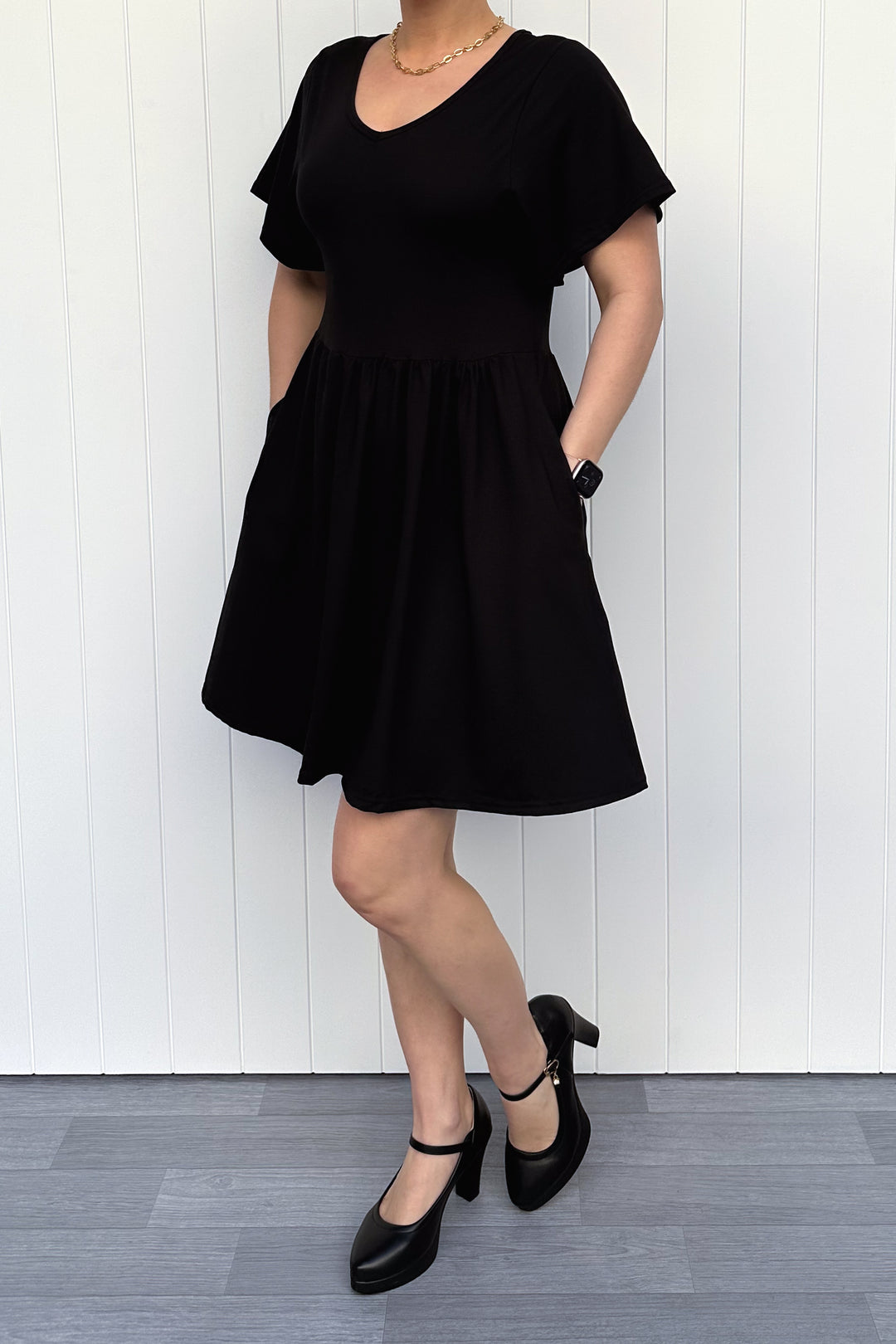 Person wearing a black dress standing against a white wooden panel background