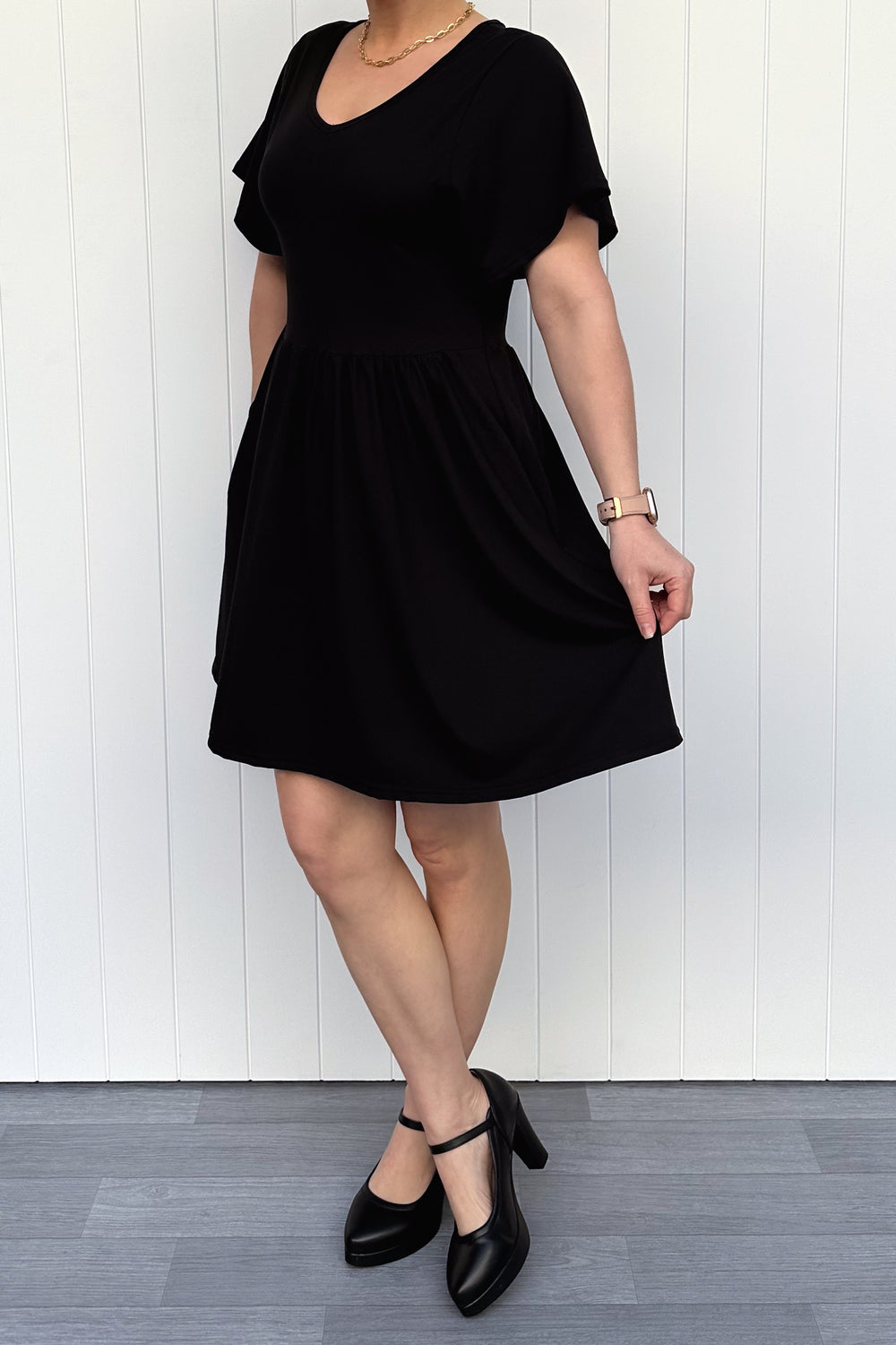 Person wearing a black dress standing against a white wooden panel background