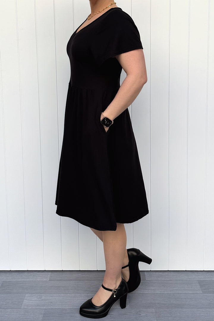 Person wearing a black dress standing against a white wooden panel background