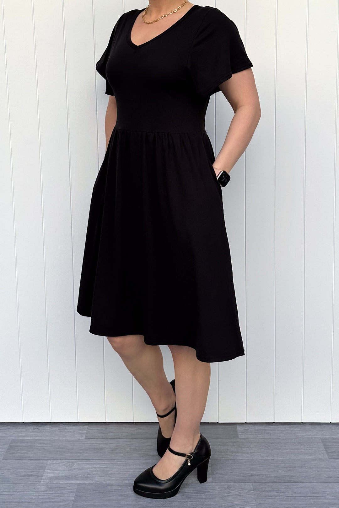 Person wearing a black dress standing against a white wooden panel background