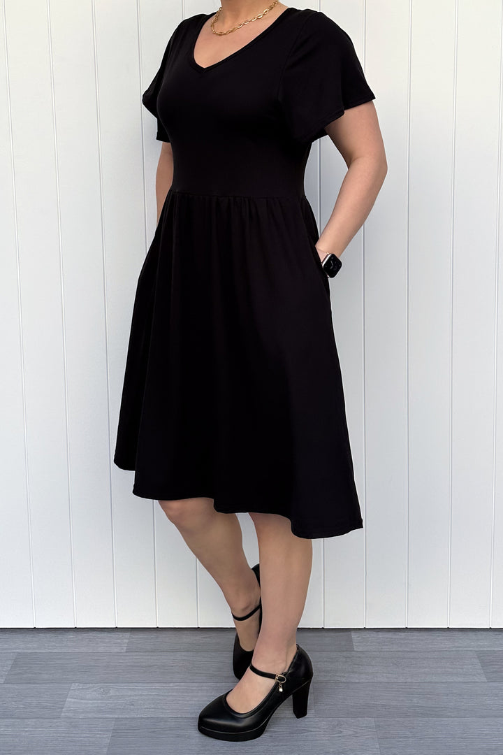 Person wearing a black dress standing against a white wooden panel background