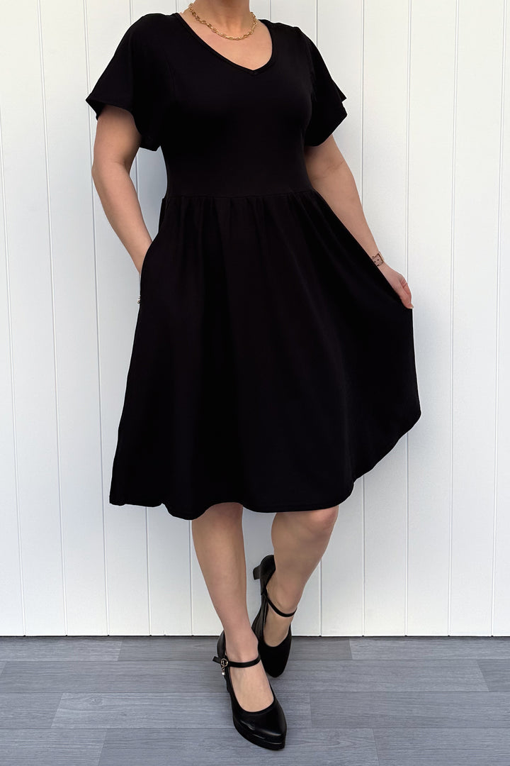 Person wearing a black dress standing against a white wooden panel background