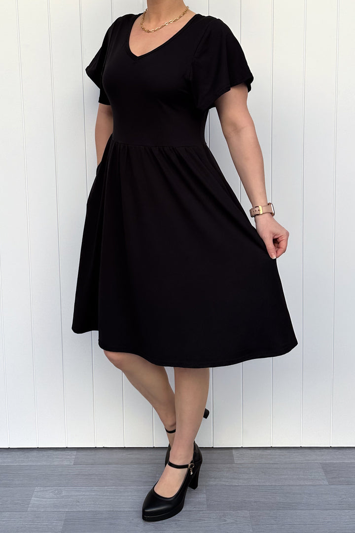 Person wearing a black dress against a white wooden panel background