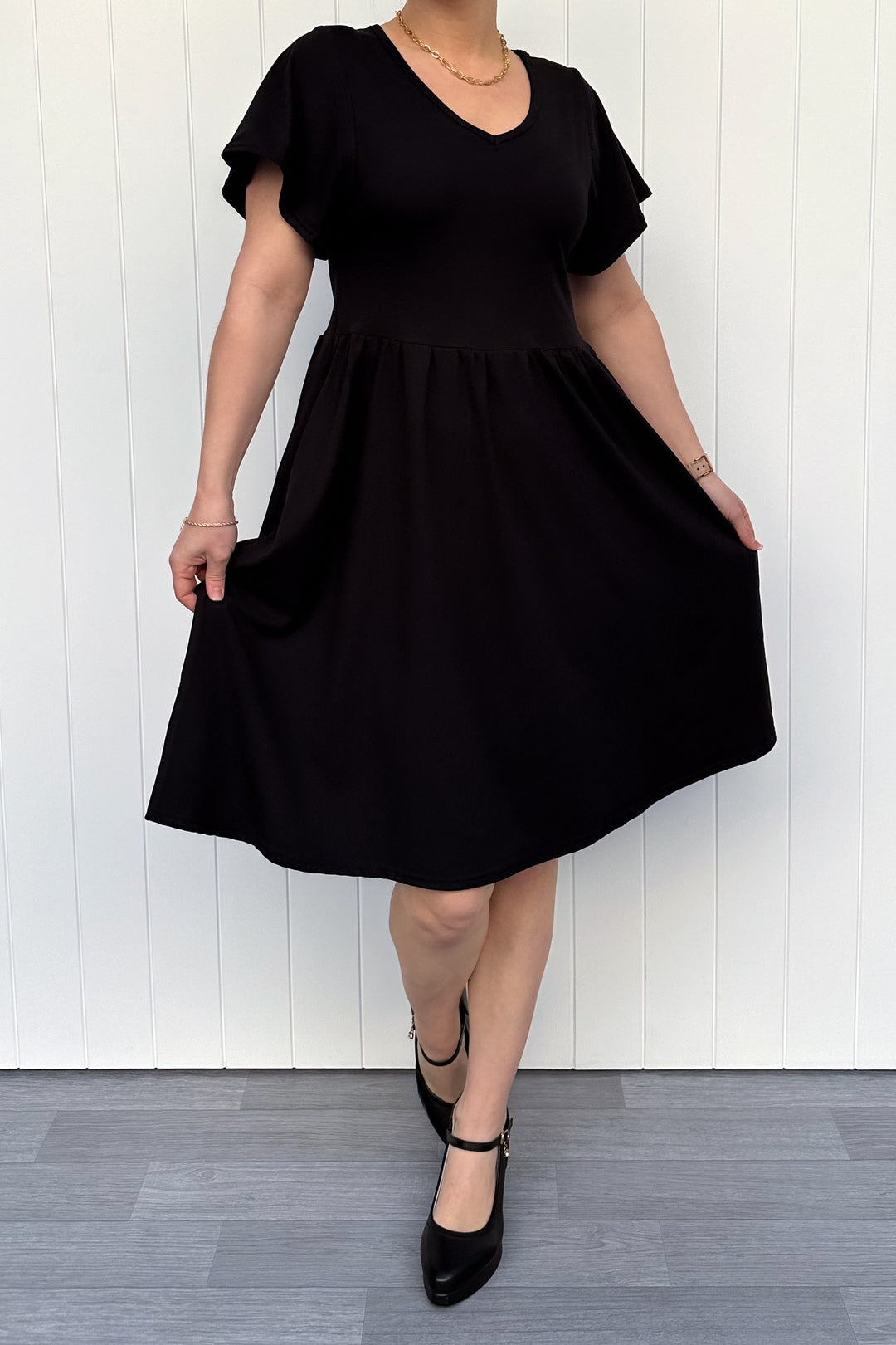 Person wearing a black dress against a white wooden panel background