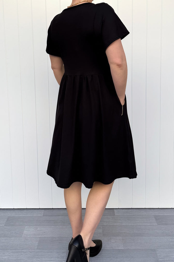 Person wearing a black dress standing against a white wall.